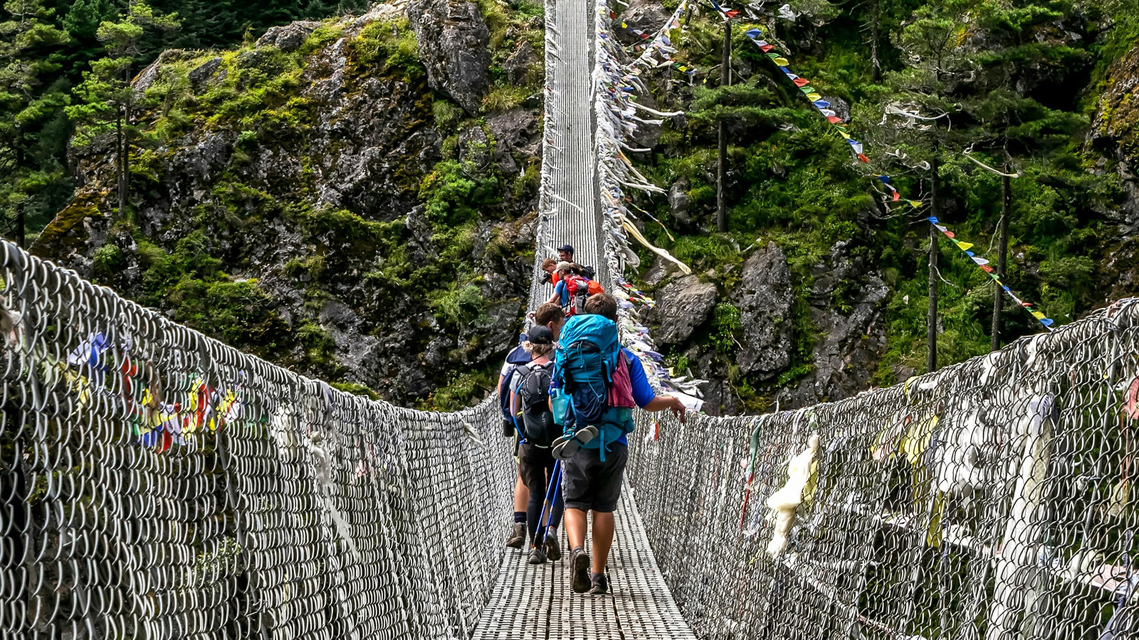 Wanderer auf Hängebrücke mit Gebetsfahnen
