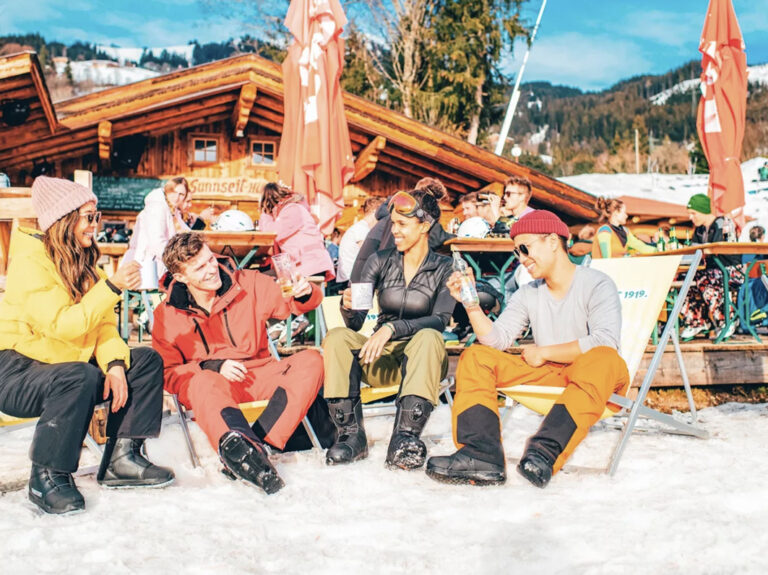 Teilnehmer sitzen mit Getränken vor Skihütte