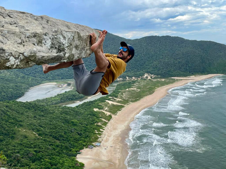 Mann hängt an Felsen hoch über einem langen Sandstrand