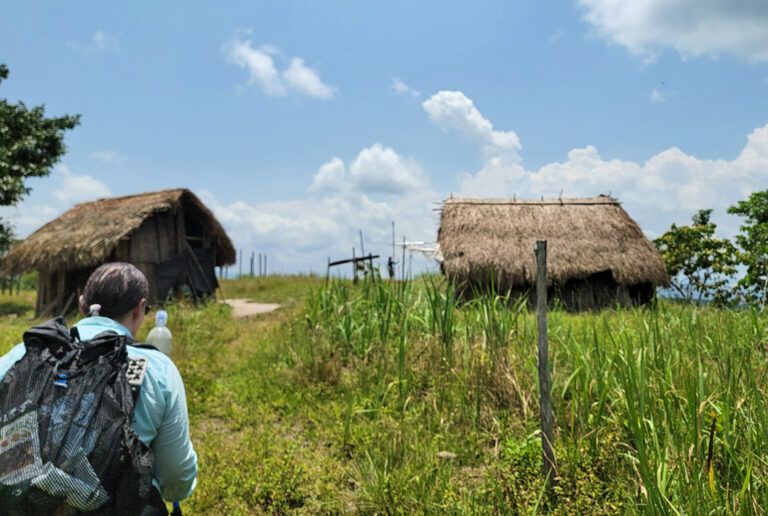 Wanderer vor strohbedeckten Hütten