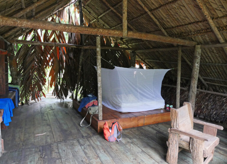 Bett mit Mosiktonetz und offener Holzüberdachung