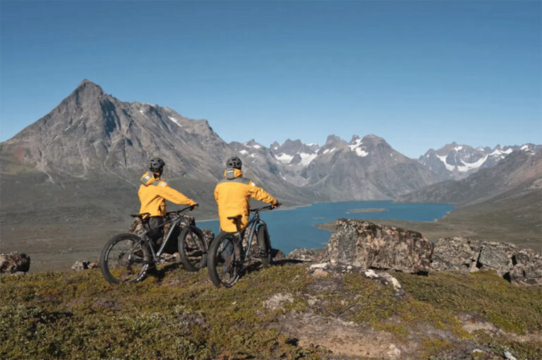 Zwei Mountainbiker blicken auf Wasser mit Bergen im Hintergrund