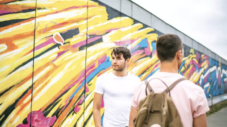 Zwei Reisende an einem bemalten Stück der Berliner Mauer