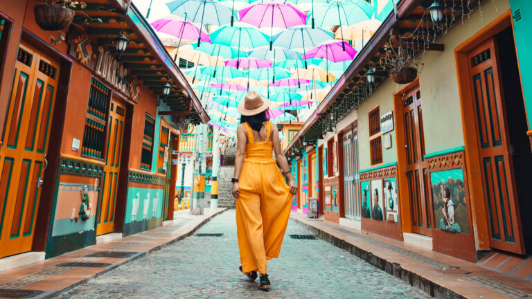 Frau von hinten läuft über eine mit Regenschirmen überspannte Kopfsteinpflasterstraße in Kolumbien