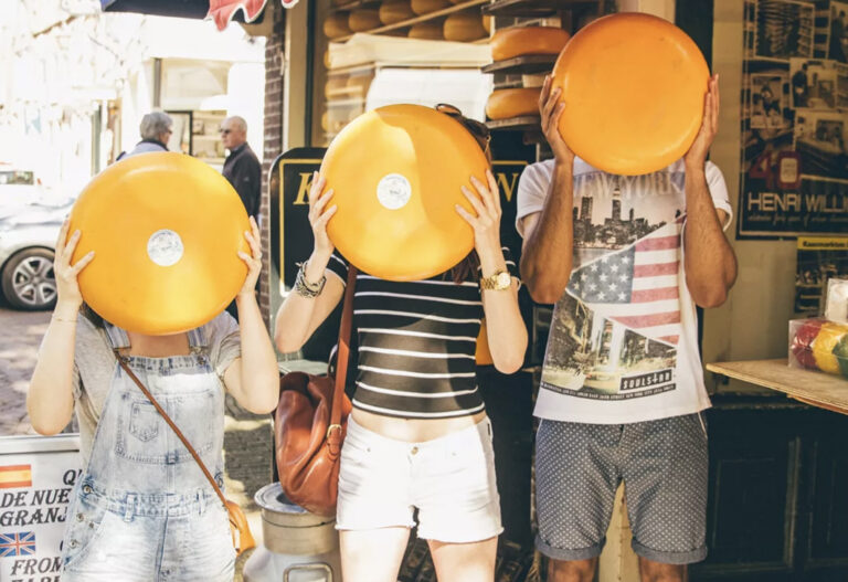 3 Touristen halten sie große runde Käsestücke vor das Gesicht