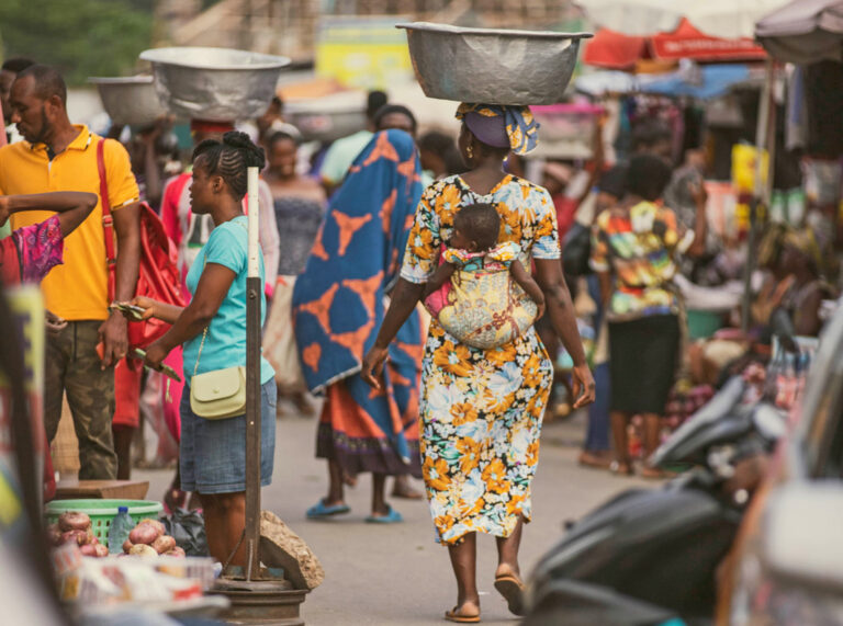 Frauen mit Baby auf dem Rücken und Wanne auf dem Kopf auf beim Markteinkauf