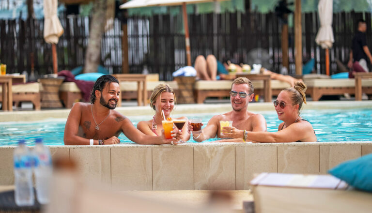 Junge Leute stoßen im Pool mit Cocktails an