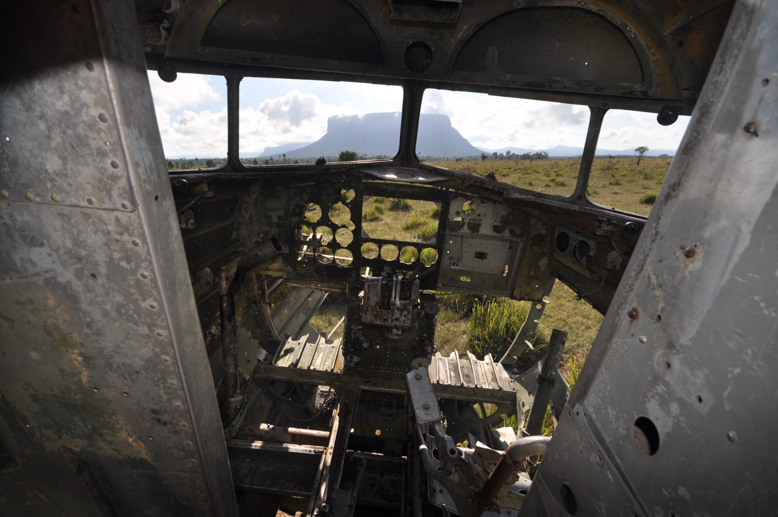 Verrostetes Flugzeugwrack in der Gran Sabana, Venezuela, umgeben von Graslandschaft mit dem Auyán-Tepui im Hintergrund.
