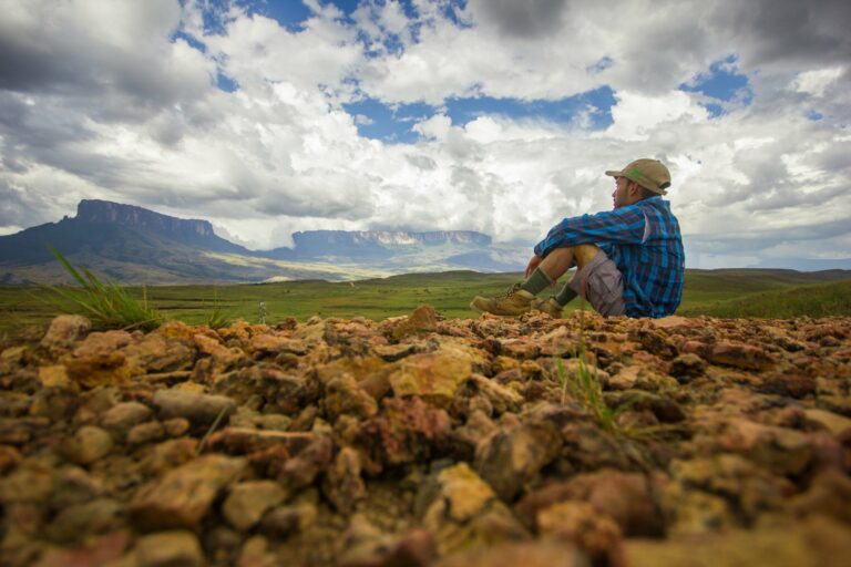 Mann sitzt auf der Erde mit Blick auf Berge - Venezuela Roraima