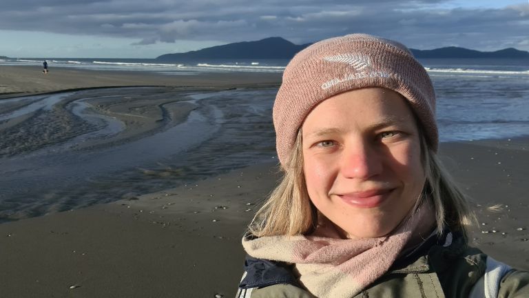 Junge Frau mit rosa Mütze und Schal am Strand im Abel Tasman Nationalpark in Neuseeland