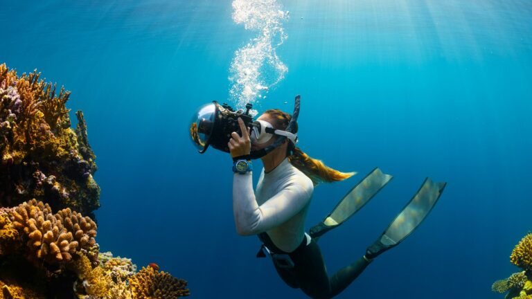 Frau taucht auf ihrer Abenteuerreise im Ozean mit einer Kamera und fotografiert Korallen